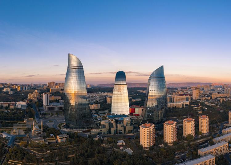 Baku the capital. Skyscrapers in the sunset light with some hills in the distance. 3 of the major skycrapers have wavy form and are made out of glass, so the reflections are visible. 