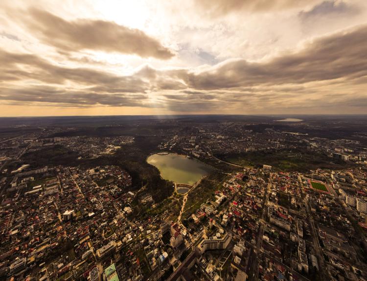 Chișinău, Moldova, picture taken from above, with a lake in the middle of the photo, buildings around it. Cloudy sky with sunshine filtered through. Flat landscape